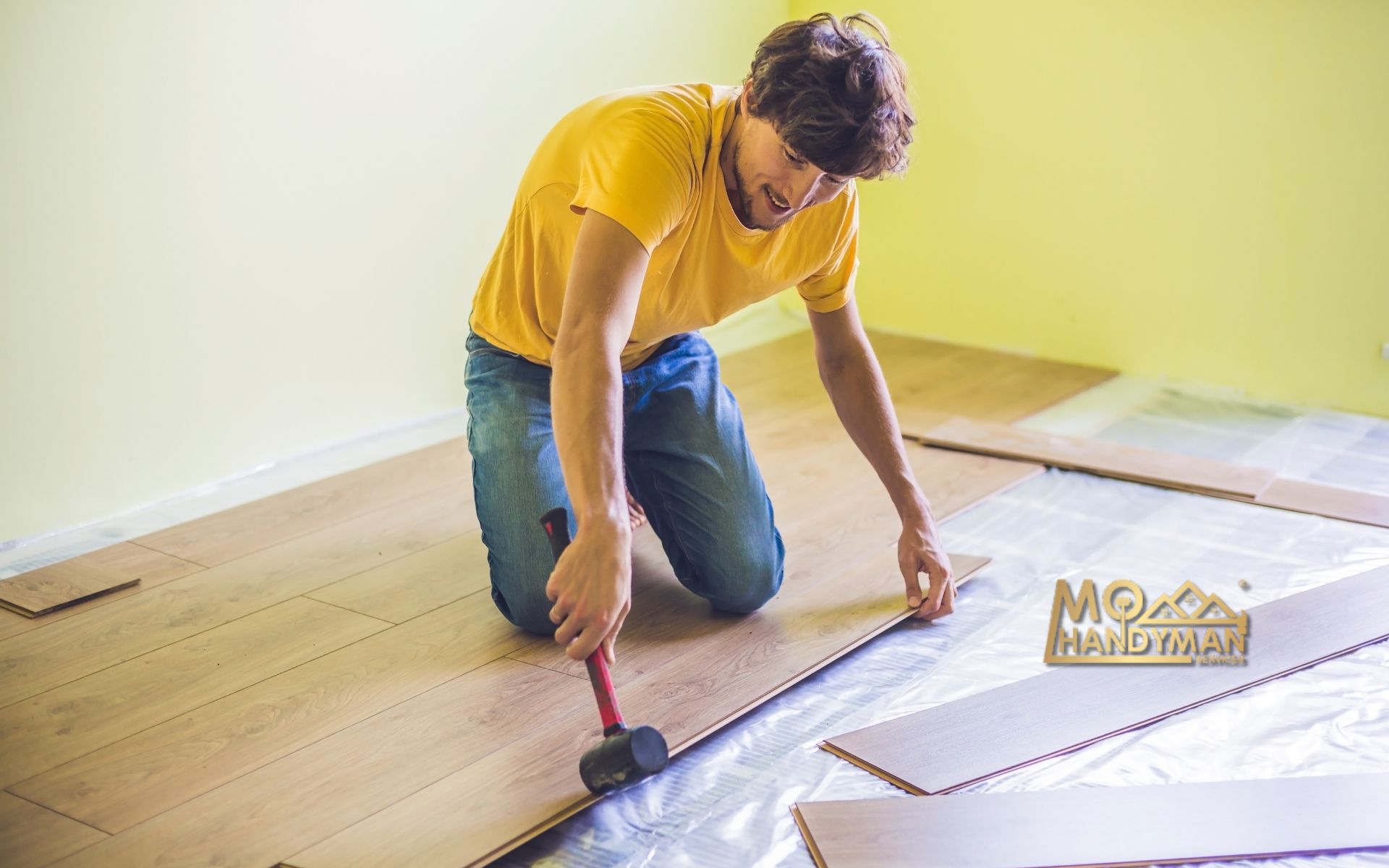 A skilled handyman in a yellow shirt meticulously installs light wooden laminate flooring, ensuring each plank fits perfectly for a flawless finish. The MoHandyman logo anchors the image, symbolizing professional and reliable flooring installation and handyman services.